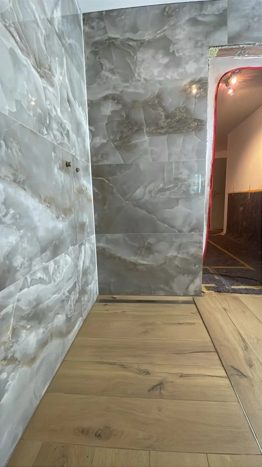 Bad während der Bauphase: fertig geflieste Wände in Onyx Greige, die Türlaibung noch offen und mit Klebeband abgeklebt, der angrenzende Boden abgedeckt.